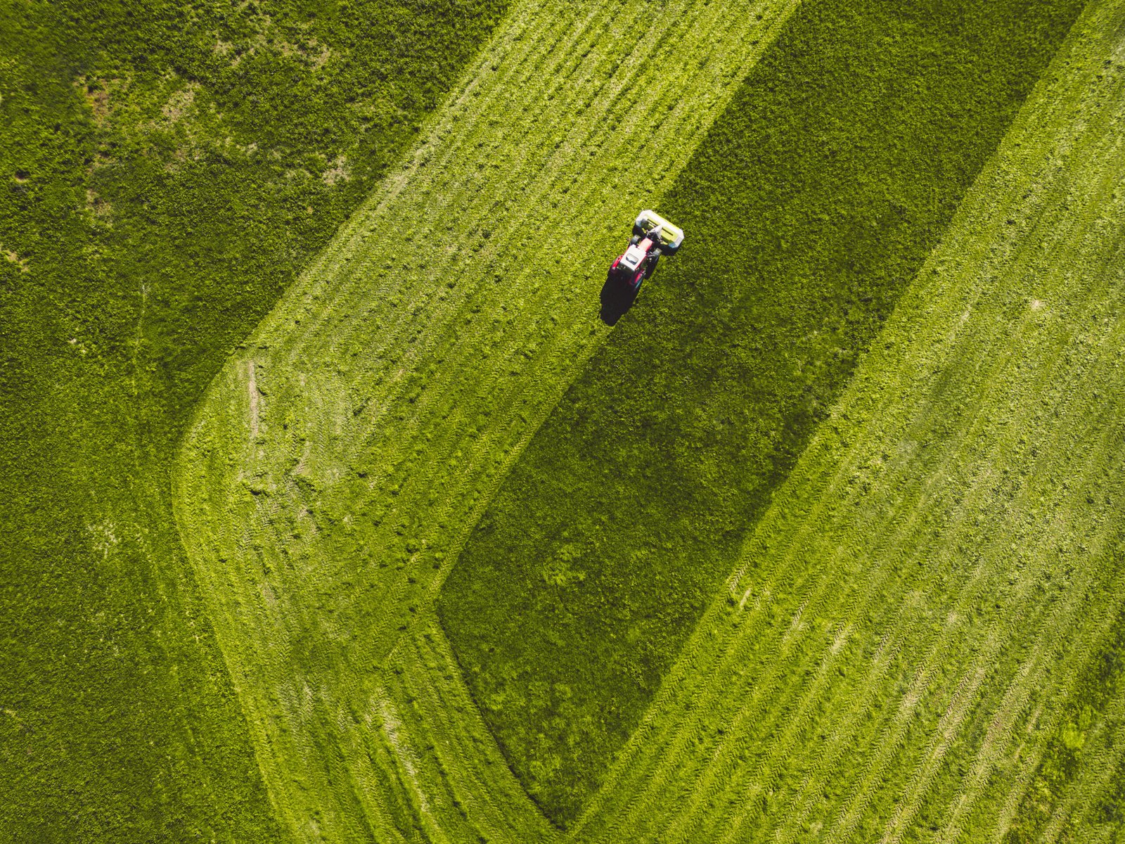 Drone photo of tractor mowing a green grass field in the countryside on a sunny day grass cutting